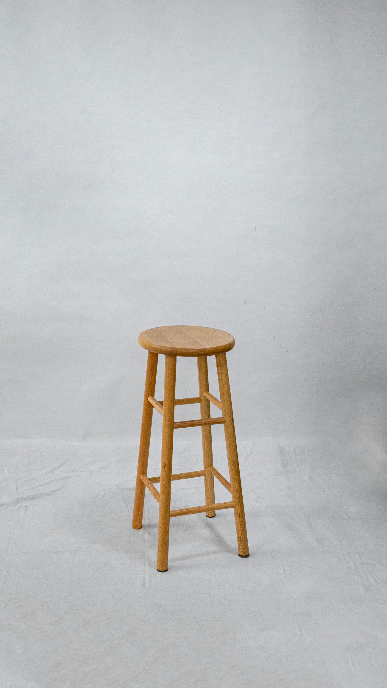 A turned wooden stool standing alone against a pale wall