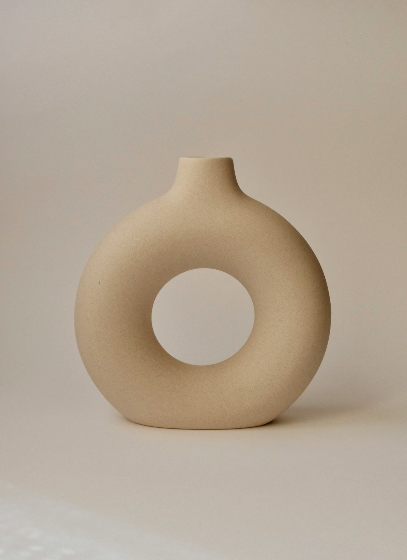 A single rounded cream coloured vase on a plain background