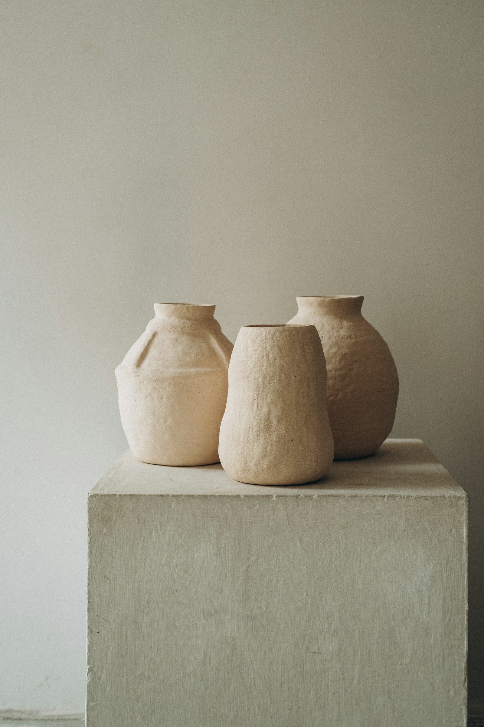 Three pale hand built clay vessels grouped on a plinth